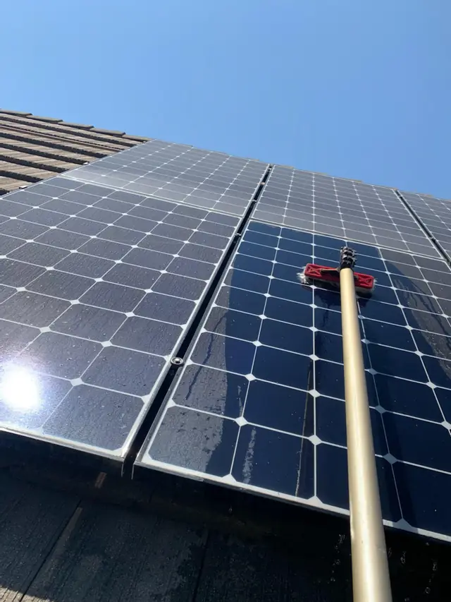Water-fed soft brush cleaning a rooftop solar panel under blue sky