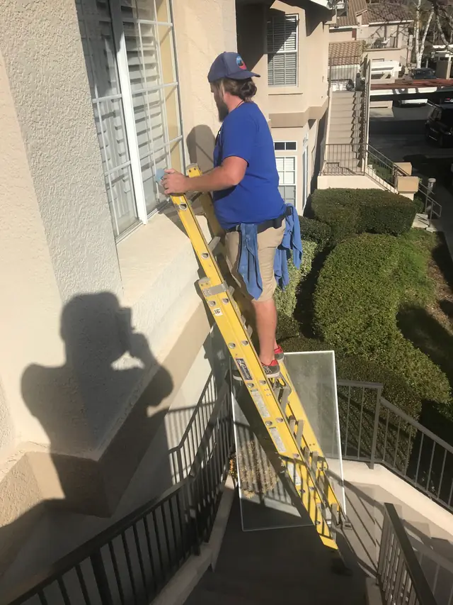 Alan's technician on a yellow ladder cleaning a second-storey window