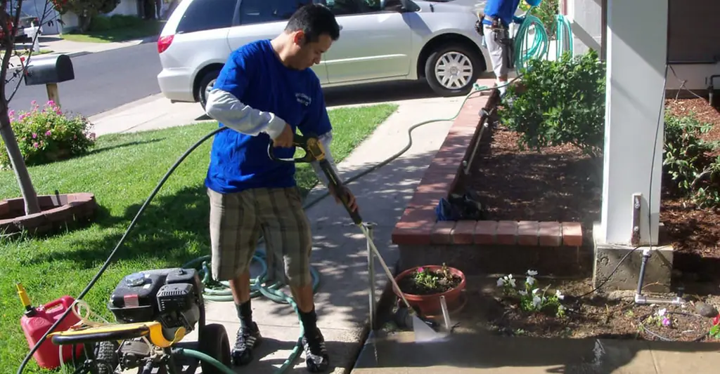 Technician pressure washing a front walkway beside a lawn